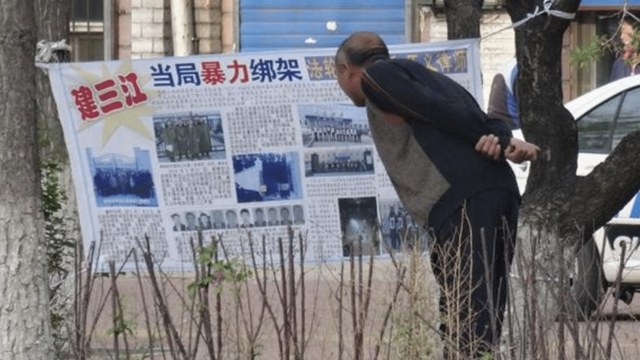 A Chinese citizen in Jiamusi, Heilongjiang Province, reads a banner hung by Falun Gong practitioners in 2018 that reads “Kidnapped by Authorities” detailing persecution cases in the area (Credit: Minghui.org)